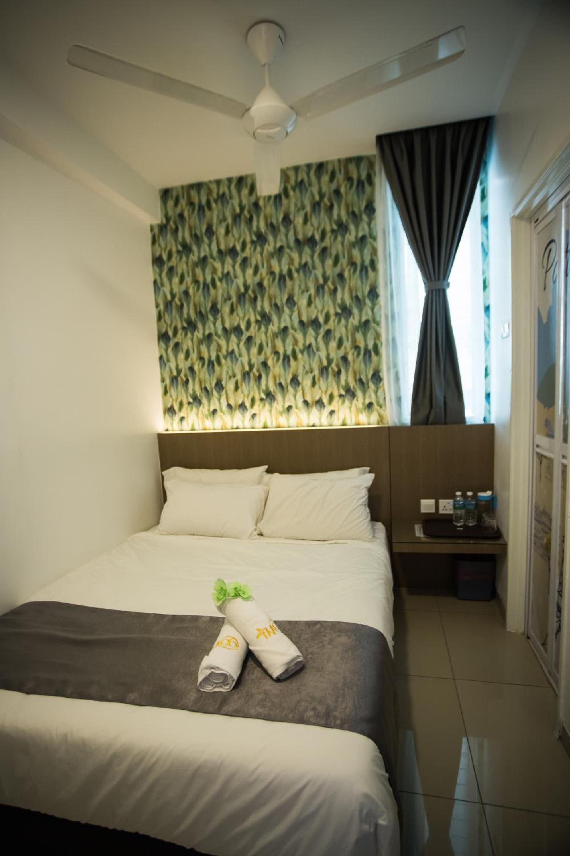 Une chambre d’hôtel avec un lit, une table de chevet, un ventilateur de plafond et un papier peint à motifs.