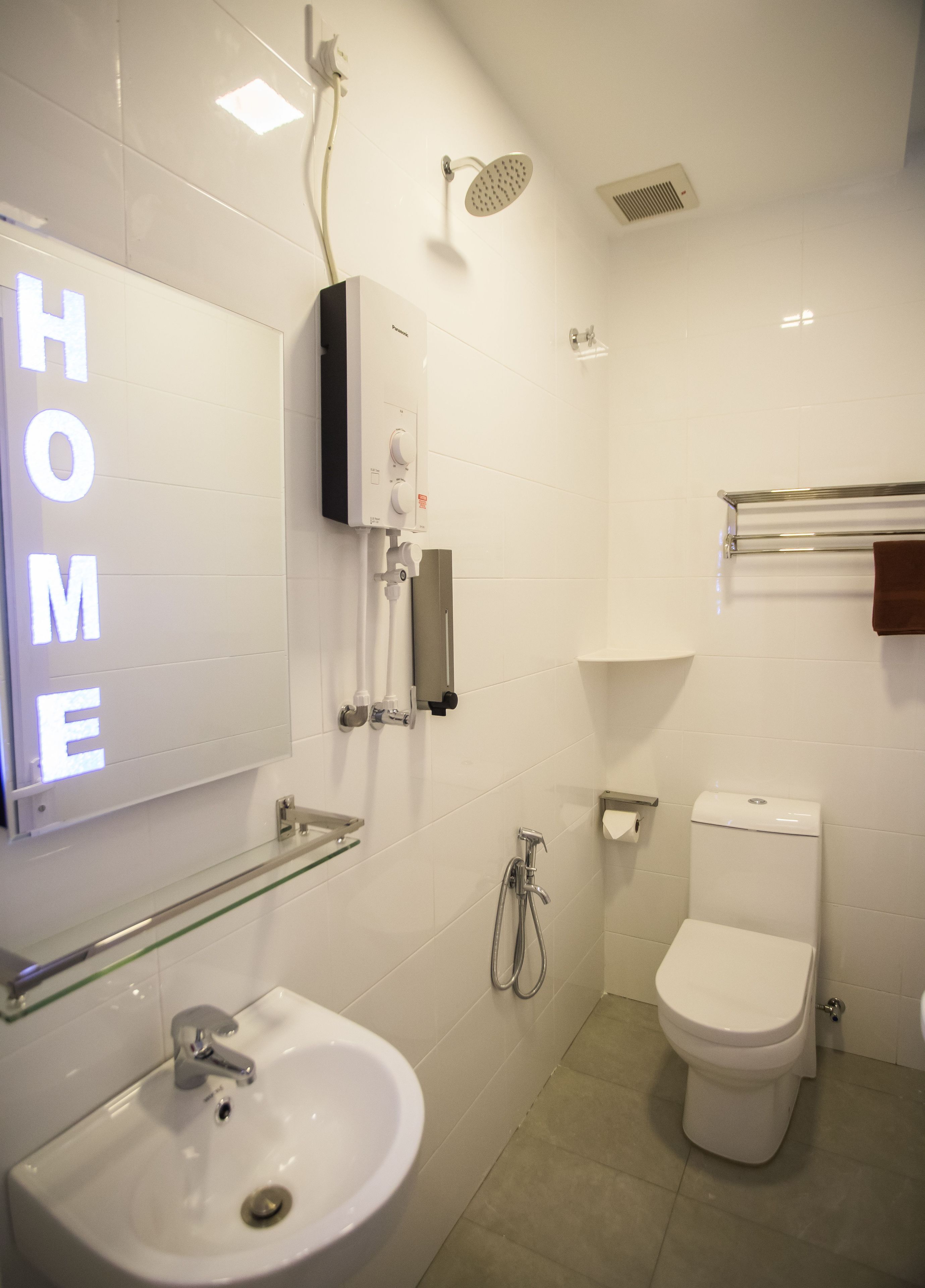 Un baño moderno con lavamanos, inodoro y ducha blancos. Hay un estante de vidrio sobre el lavamanos y un perchero encima del inodoro.