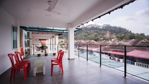 A balcony with red chairs, a table, and a ceiling fan. It overlooks a residential area with houses and a hill. - IM 96 Villa (Kuantan)