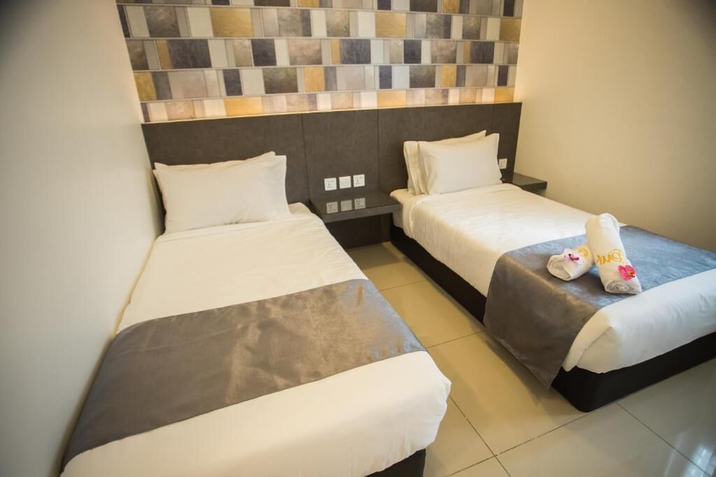 A hotel room with two single beds, a tiled wall, and a small nightstand with a lamp.