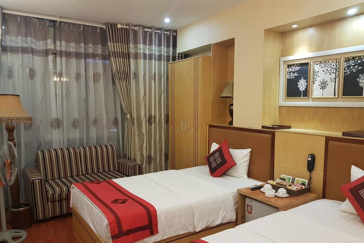 Habitación de hotel con dos camas, un sofá, un armario y una ventana con paneles decorativos.