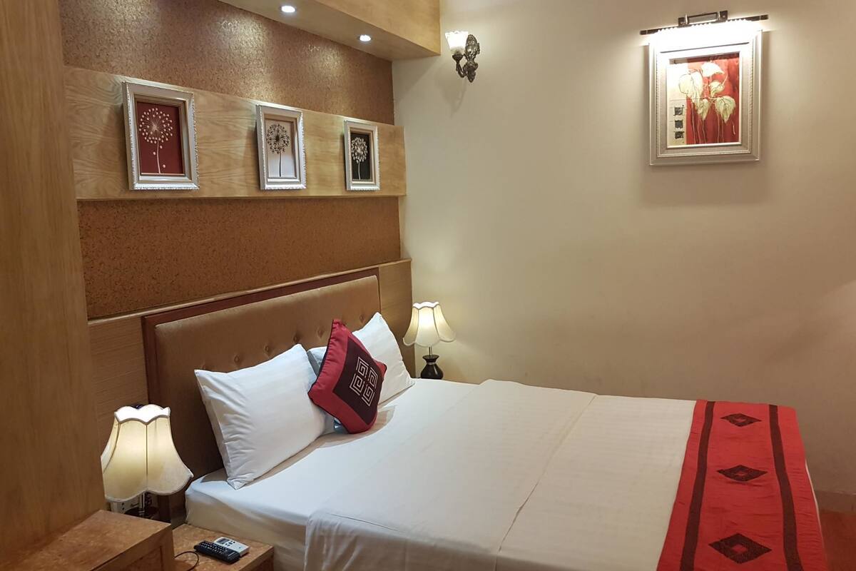 Una habitación de hotel con una cama, lámparas de noche, una mesita de noche y obras de arte colgadas en la pared.