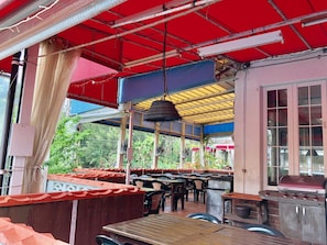 An outdoor restaurant with wooden tables and chairs, a barbecue grill, and a red canopy. - Key West Club Okinawa (Onna)