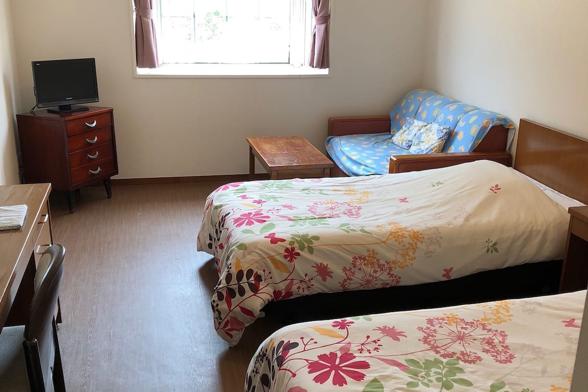 Un dormitorio con dos camas, un escritorio, una silla, una mesita y una ventana con cortinas.