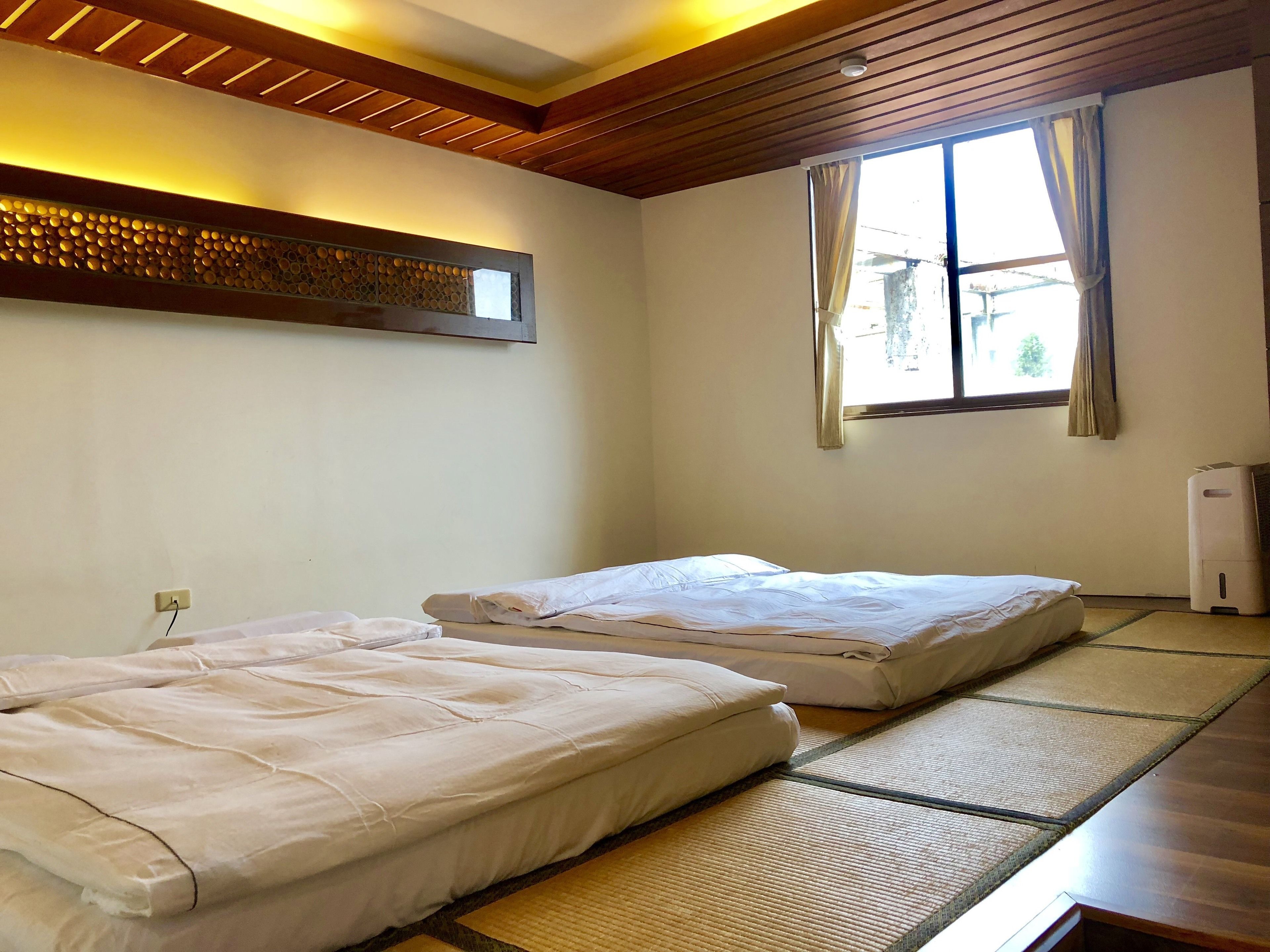 Een kamer met twee bedden, een raam met gordijnen, een wandairconditioner en een plafond met houten balken.