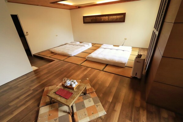 Una habitación con dos camas, una mesita con mantel rojo y un calentador fijado a la pared.