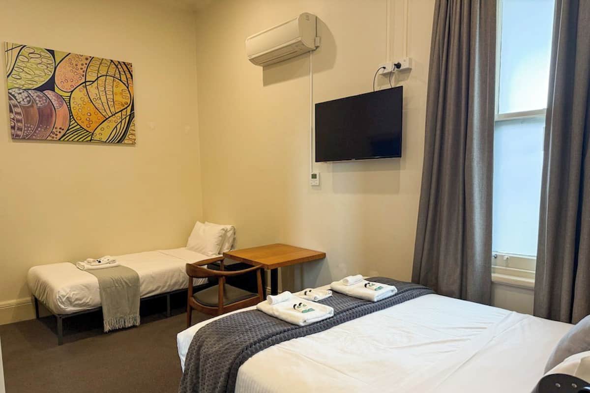 A hotel room with two single beds, a TV, an air conditioner, and a painting on the wall.