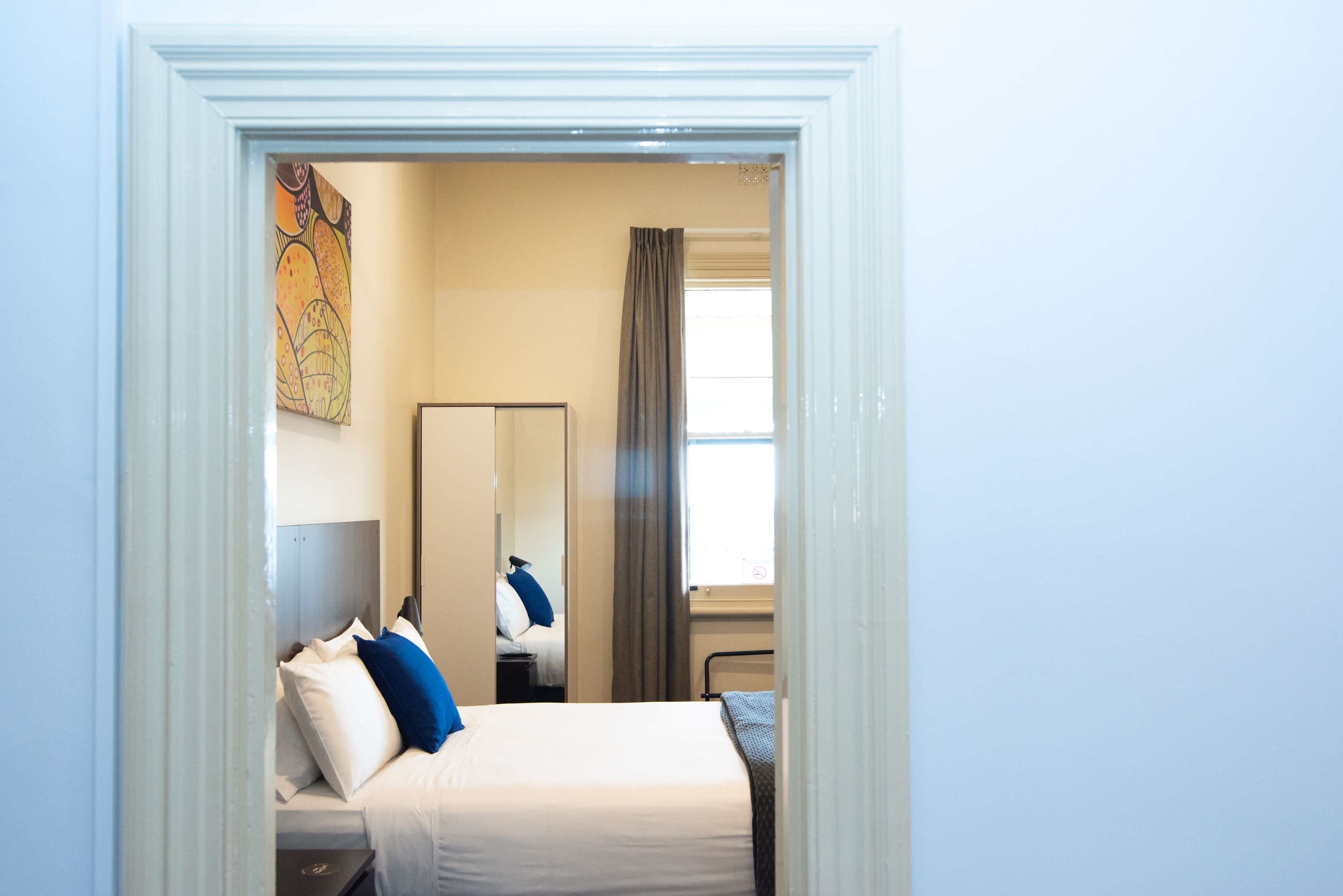 A hotel room with a bed, a nightstand, a mirror, a window with curtains, and a painting on the wall.