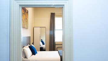 A hotel room with a bed, a nightstand, a mirror, a window with curtains, and a painting on the wall.