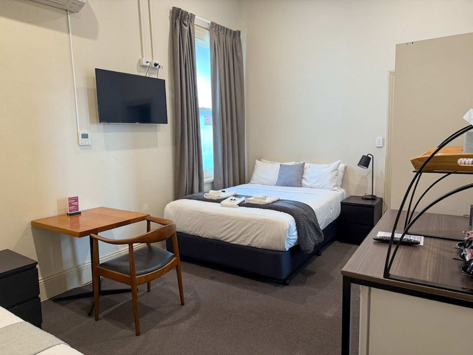 Una camera d'albergo con un letto, una scrivania, una sedia, una TV a muro e una finestra con tende.