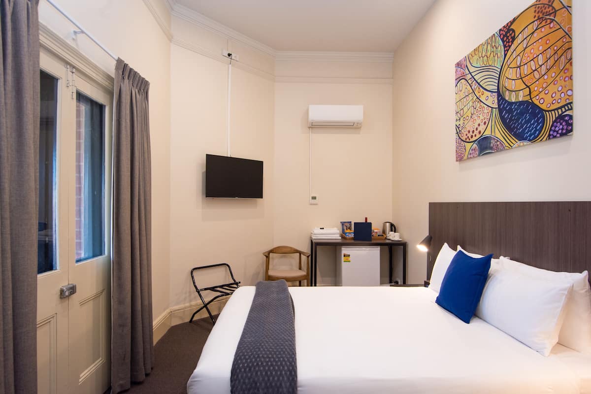A hotel room with a bed, a desk, a chair, an air conditioner, and a television.