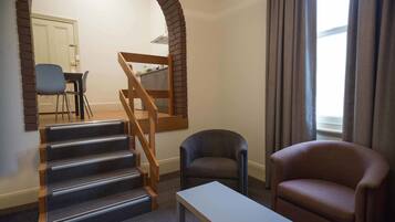 Una sala de estar con una escalera, un sofá, una mesa y vistas a una cocina y comedor.