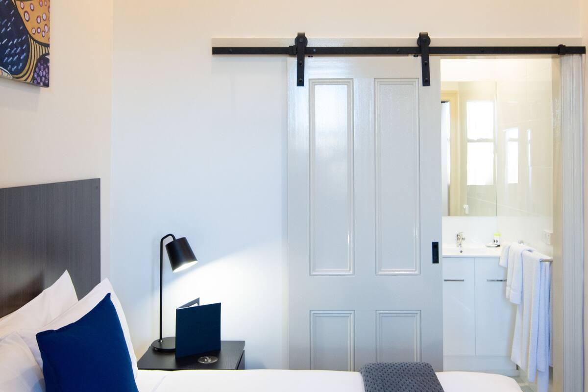 A hotel room with a bed, a nightstand, a lamp, a sliding door, and a bathroom visible through the door.