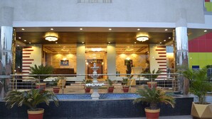 Een hotel lobby met een fontein, potplanten en een receptiebalie.