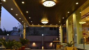 Een hotellobby met een modern design, met een grote kroonluchter, potplanten en een trap naar de bovenverdieping.