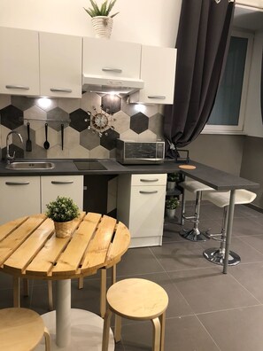 A modern kitchen with a microwave, sink, and a round wooden table with stools. - La Casa di Ulisse (Naples)