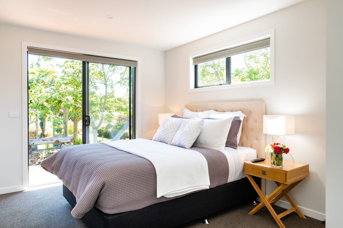 A bedroom with a bed, a nightstand, a lamp, and a window.