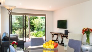 Een moderne woonkamer met een glazen tafel, grijze banken en een televisie aan de muur.