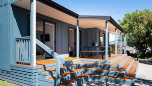 Een modern huis met een overdekte veranda, houten treden en uitzicht op de achtertuin.