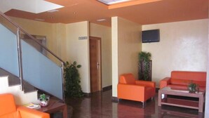 A lobby with a staircase, orange seating, a flat-screen TV, and a sign for 'SERVICIOS'.