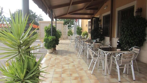 A covered outdoor seating area with metal chairs and tables, potted plants, and a tiled floor.