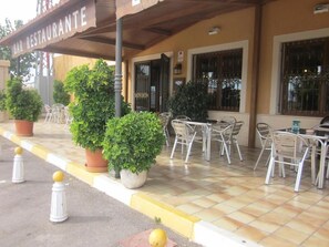 Un espace extérieur aménagé avec des tables et des chaises, des plantes en pot et une enseigne indiquant « BAR RESTAURANT ».