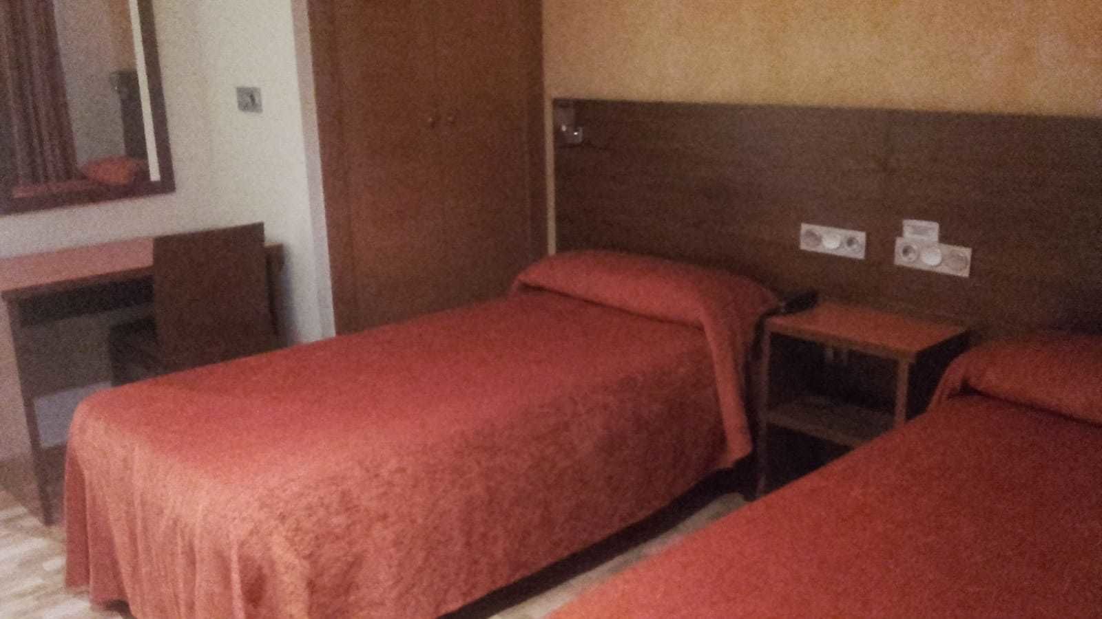 A room with two single beds, a wooden headboard, a small bedside table, and a mirror on the wall.
