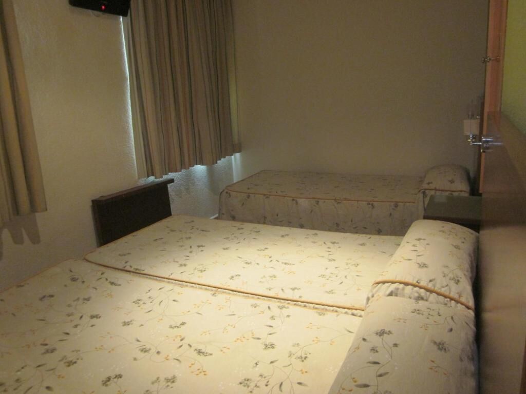 A room with two beds, a window with curtains, a radiator, and a door.