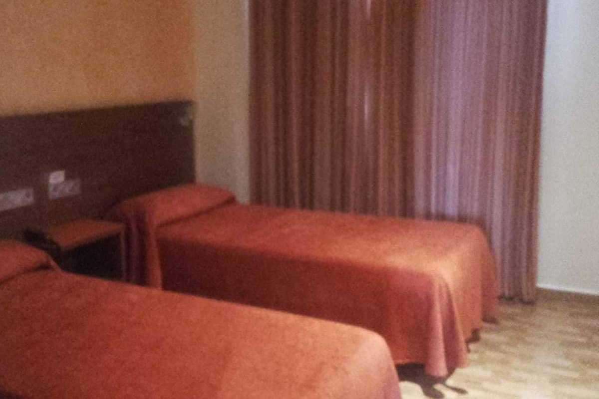 Une chambre avec deux lits simples, une tête de lit en bois et un rideau.