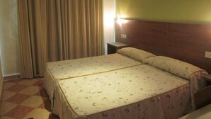 A double bed with floral bedding, a wooden headboard, a nightstand, and a curtain.