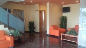 A lobby with a staircase, orange seating, and a TV on the wall.