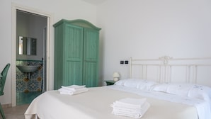 A neatly made bed with folded towels, a green wardrobe, a bathroom with a sink and mirror, and a white headboard. - Affittacamere Il Melograno (Pollica)