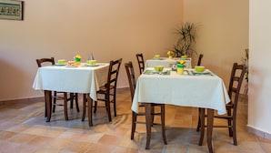 A dining area with two tables, each covered with a white tablecloth, surrounded by wooden chairs. - Affittacamere Il Melograno (Pollica)