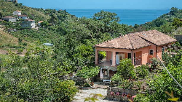 A coastal house with a tiled roof, surrounded by lush greenery and a view of the sea. - Affittacamere Il Melograno (Pollica)