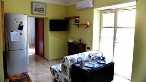 A compact kitchen with a refrigerator, a flat-screen TV, and a dining area with a table set for two. - La Fenice Punto Zero (Naples)