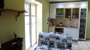 A compact living space with a kitchenette, a sofa with a patterned cover, and a sliding glass door leading to an outdoor area. - La Fenice Punto Zero (Naples)