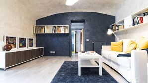 Una sala de estar moderna con una pared curva, un sofá blanco con almohadones amarillos, una mesa de centro blanca y una estantería.