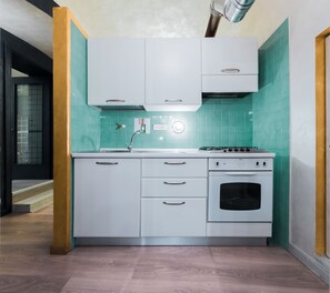 Een compacte keuken met witte kastjes, een gasfornuis en een ingebouwde oven.