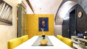 Un comedor con una mesa blanca, sillas amarillas, un bol y un reloj en la pared.
