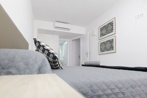 A bedroom with a bed, a pillow, a wall-mounted air conditioner, and two framed pictures.
