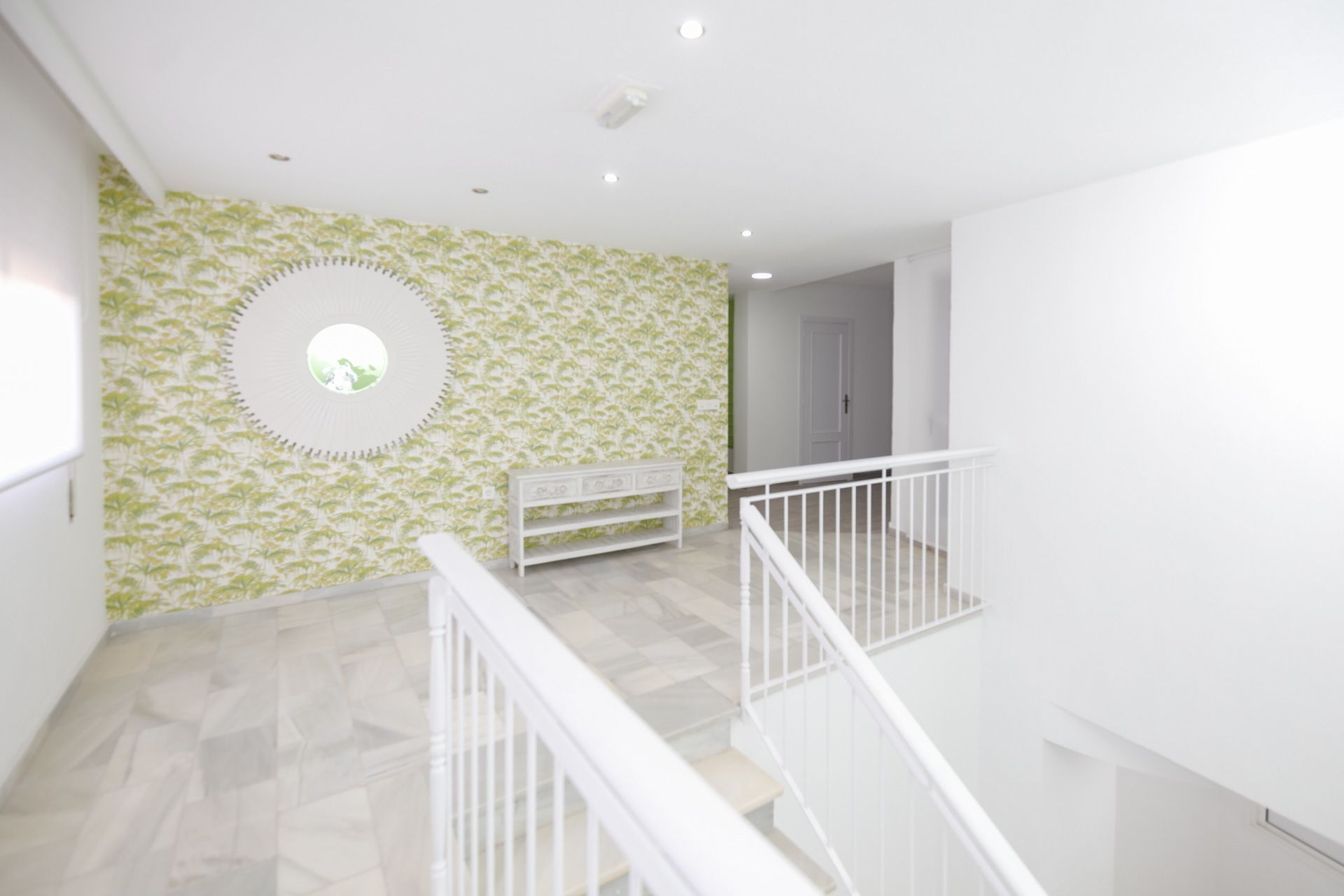 A spacious hallway with a patterned wall, a white bench, and a staircase with a white railing.