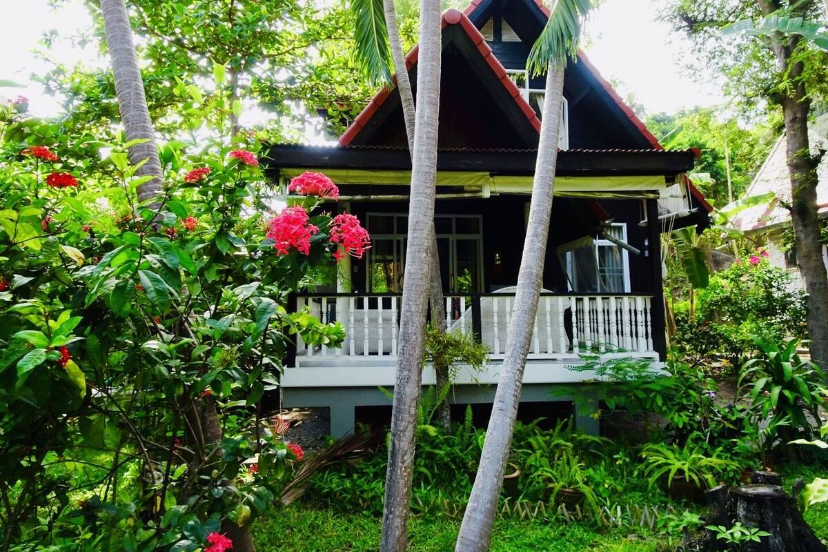 A house surrounded by lush greenery and red flowers.