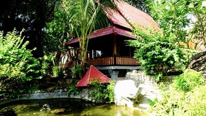 A traditional wooden structure with a red roof, surrounded by lush greenery and a small pond with koi fish. - Starbay Samui (Koh Samui)