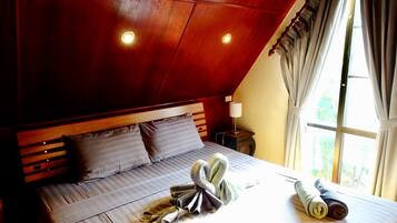 Una camera da letto con soffitto a falde, una testiera in legno, un letto con biancheria grigia, due cuscini, una lampada da comodino e una finestra con tende.