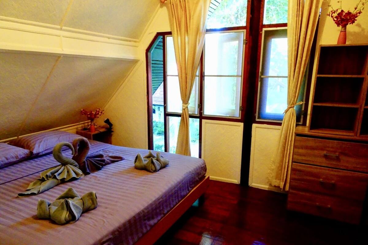 A bedroom with a bed, a wooden dresser, and a window with curtains.