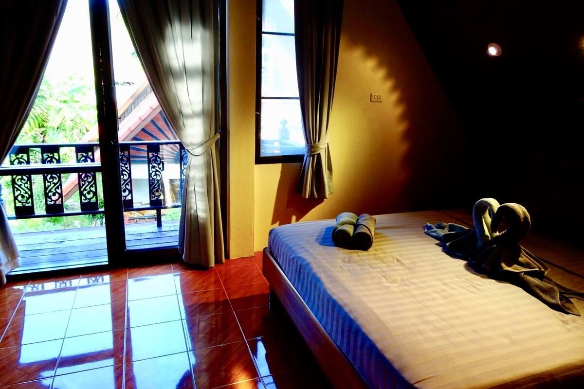 A bedroom with a bed, curtains, a window, and a view of a balcony.