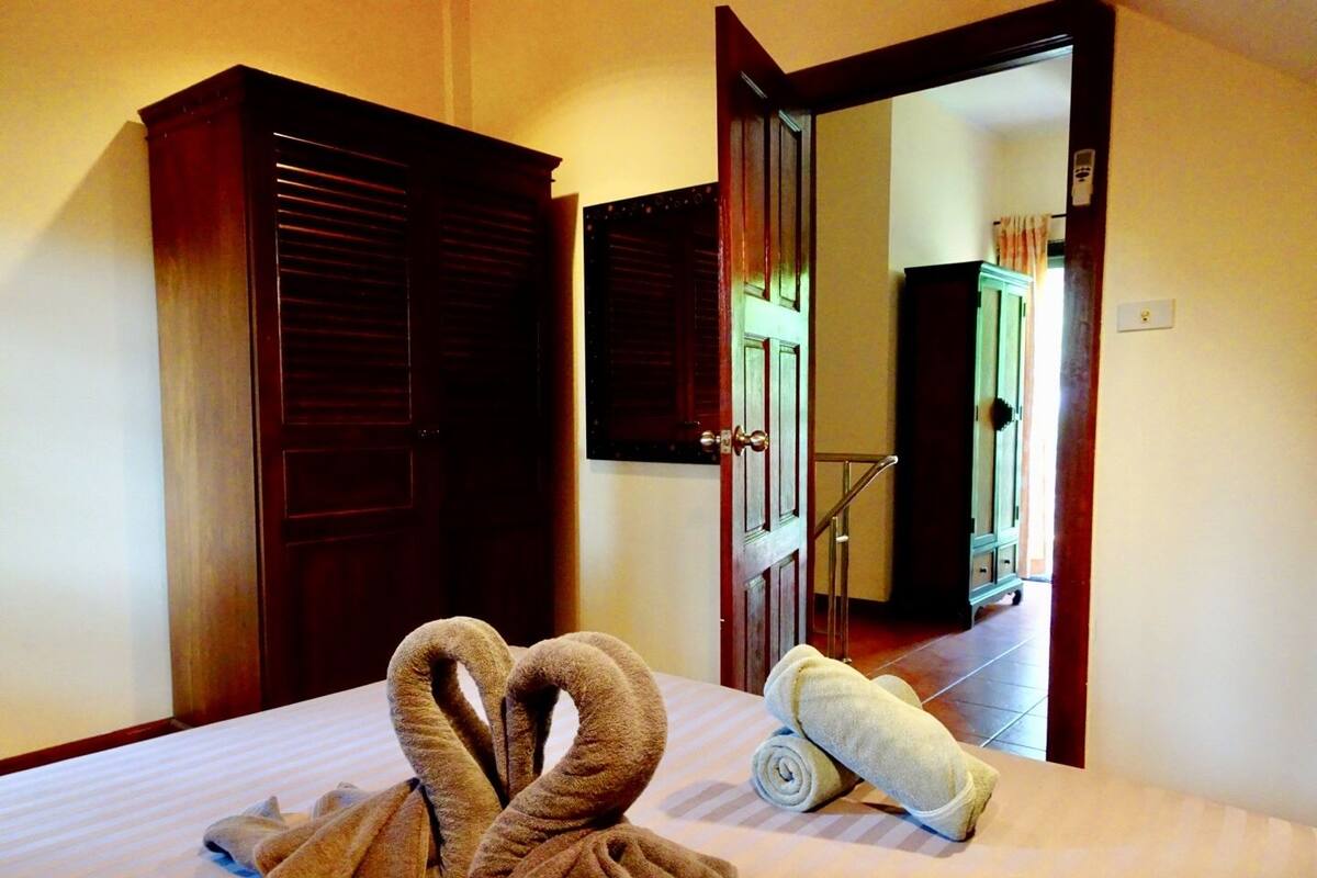 A hotel room with a bed, two brown towels arranged in a heart shape, and a rolled white towel on the bed.