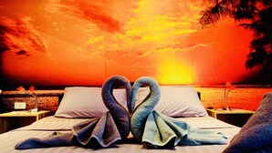 A bed with towels arranged in a heart shape, a nightstand with a lamp, and a view of the sunset over the ocean. - Starbay Samui (Koh Samui)