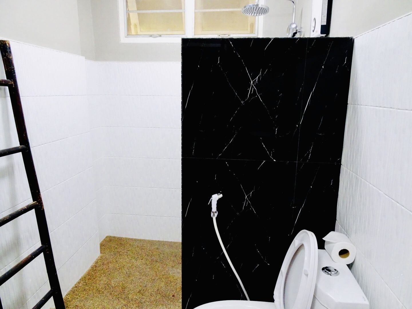 A bathroom with white tiled walls, a black marble shower enclosure, a white toilet, and a showerhead.