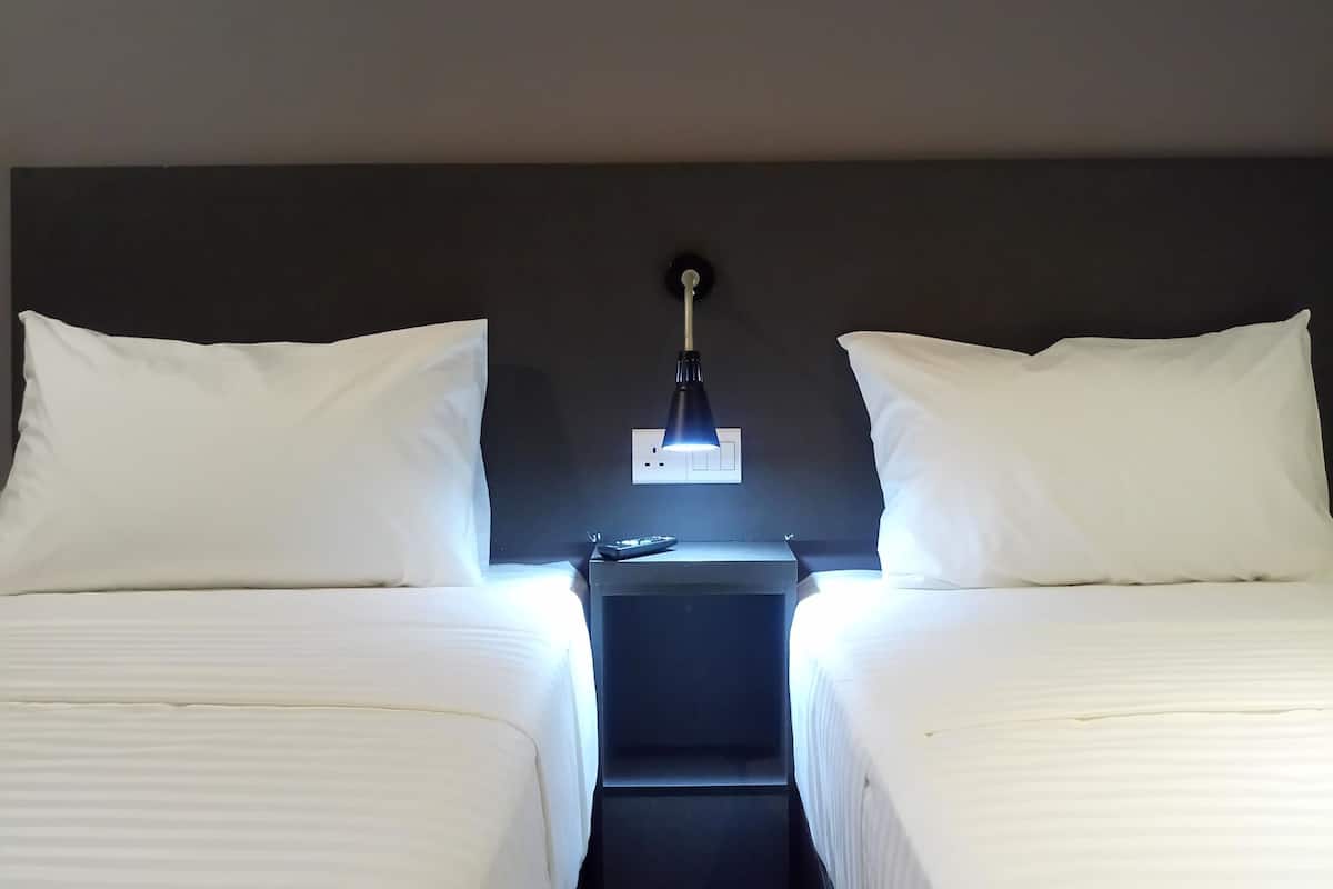 A room with two beds, a nightstand, and a wall-mounted lamp.